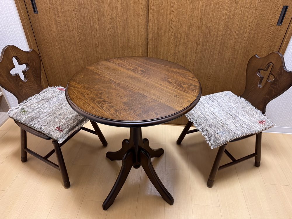 木の丸テーブルと、手織りのクッションを置いた椅子ふたつ
