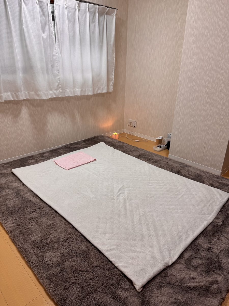 施術用のマット。白い敷きパッドとピンクのタオル、足元に小さな灯り